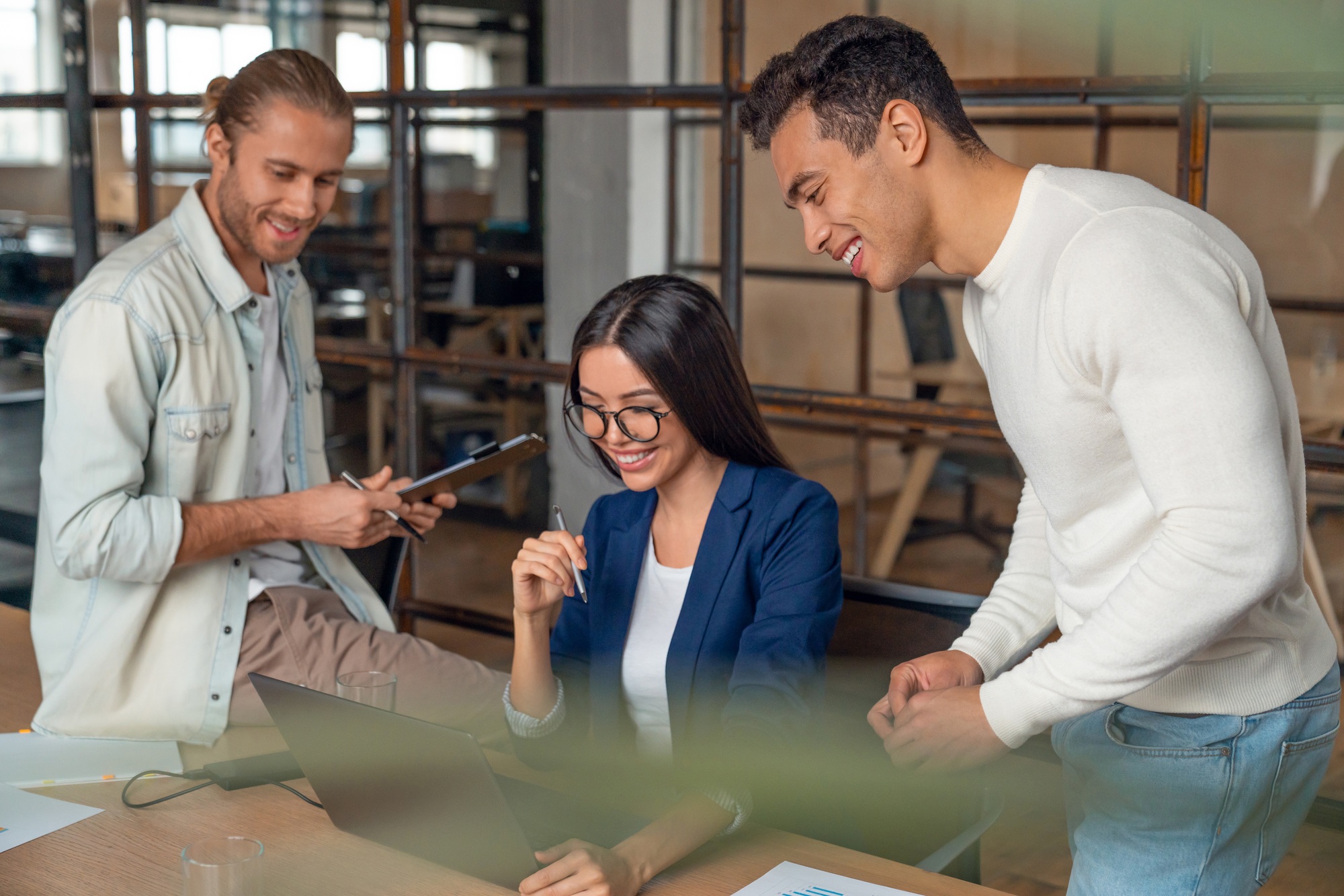 Smiling asian woman giving presenting over laptop to colleagues in meeting room.