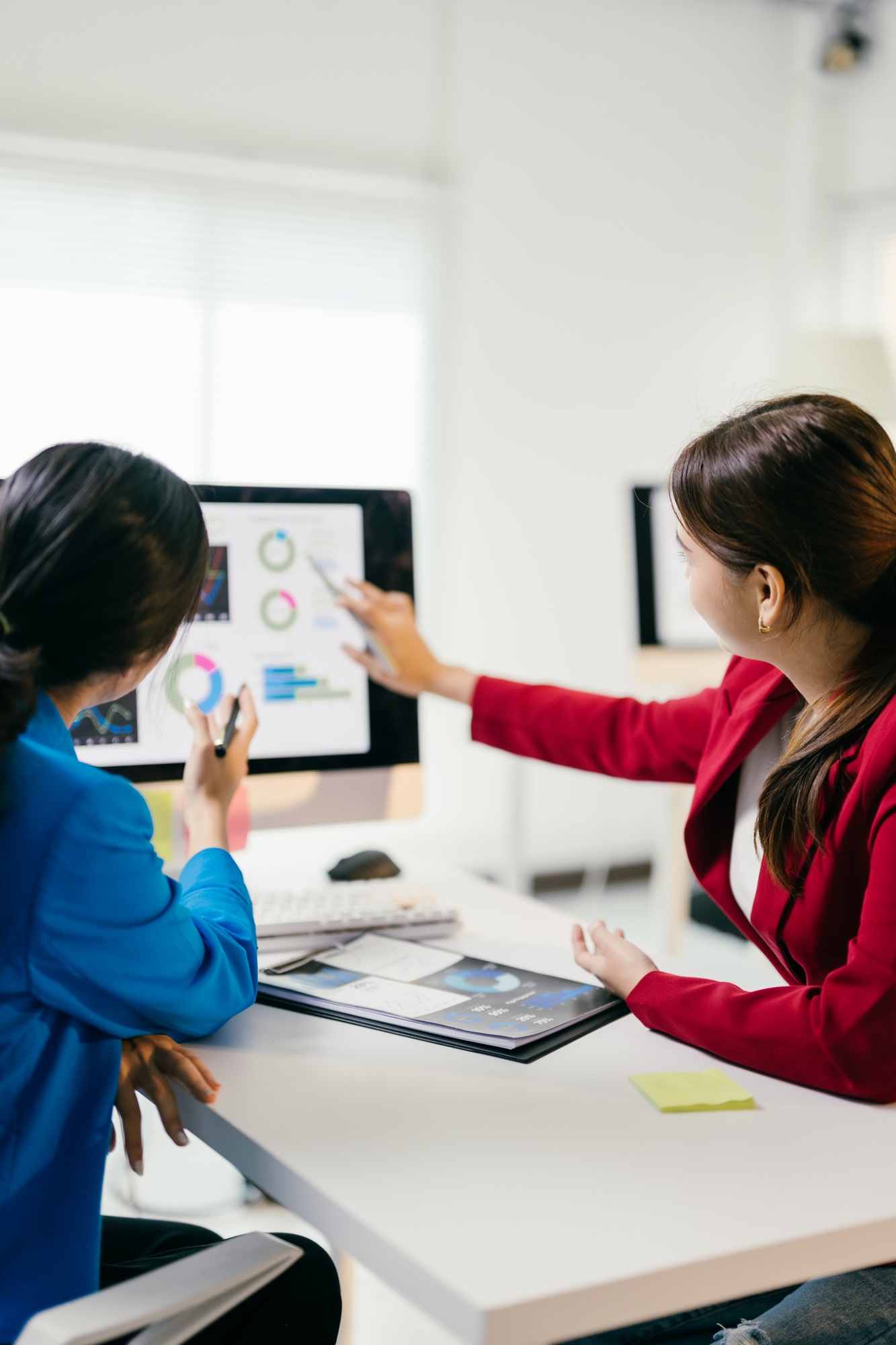 Two businesswomen discussing financial data on a computer, strategizing for the future with teamwork